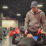Personal trainer spotting woman during incline dumbbell chest press.