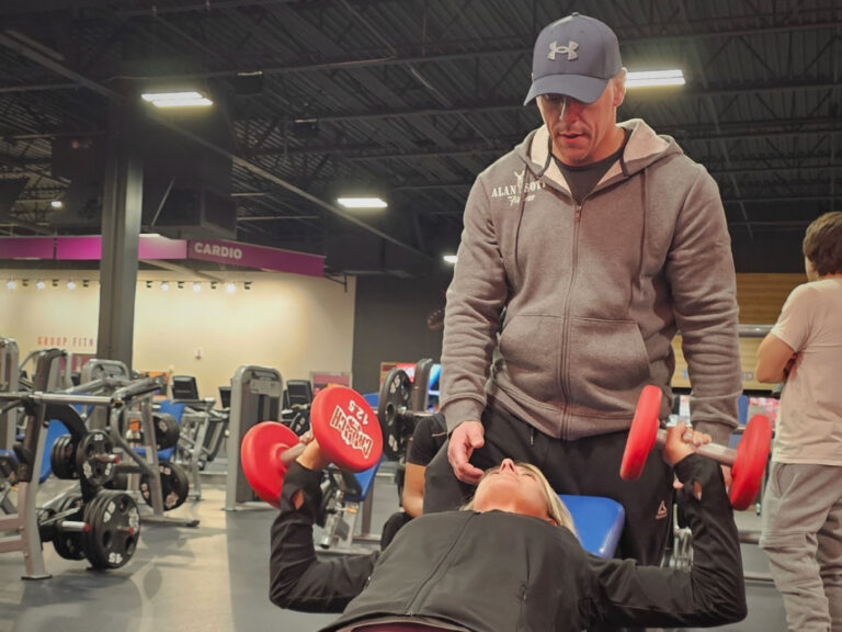 Personal trainer spotting woman during incline dumbbell chest press.